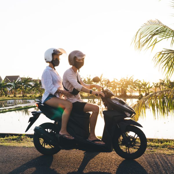 Side view of full length anonymous couple in masks and helmets driving motorcycle and chilling in hot country while spending summer vacation together