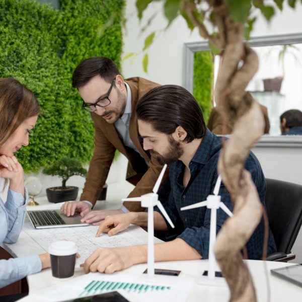 Smart qualified skilled young engineers looking at the project of alternative energy with miniatures of windmill turbines at the table.