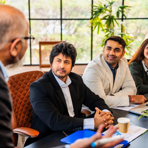 Indian Asian senior business professional or CEO presenting strategy on a glass board or delivering a motivational speech to his young team during a meeting in a corporate conference room