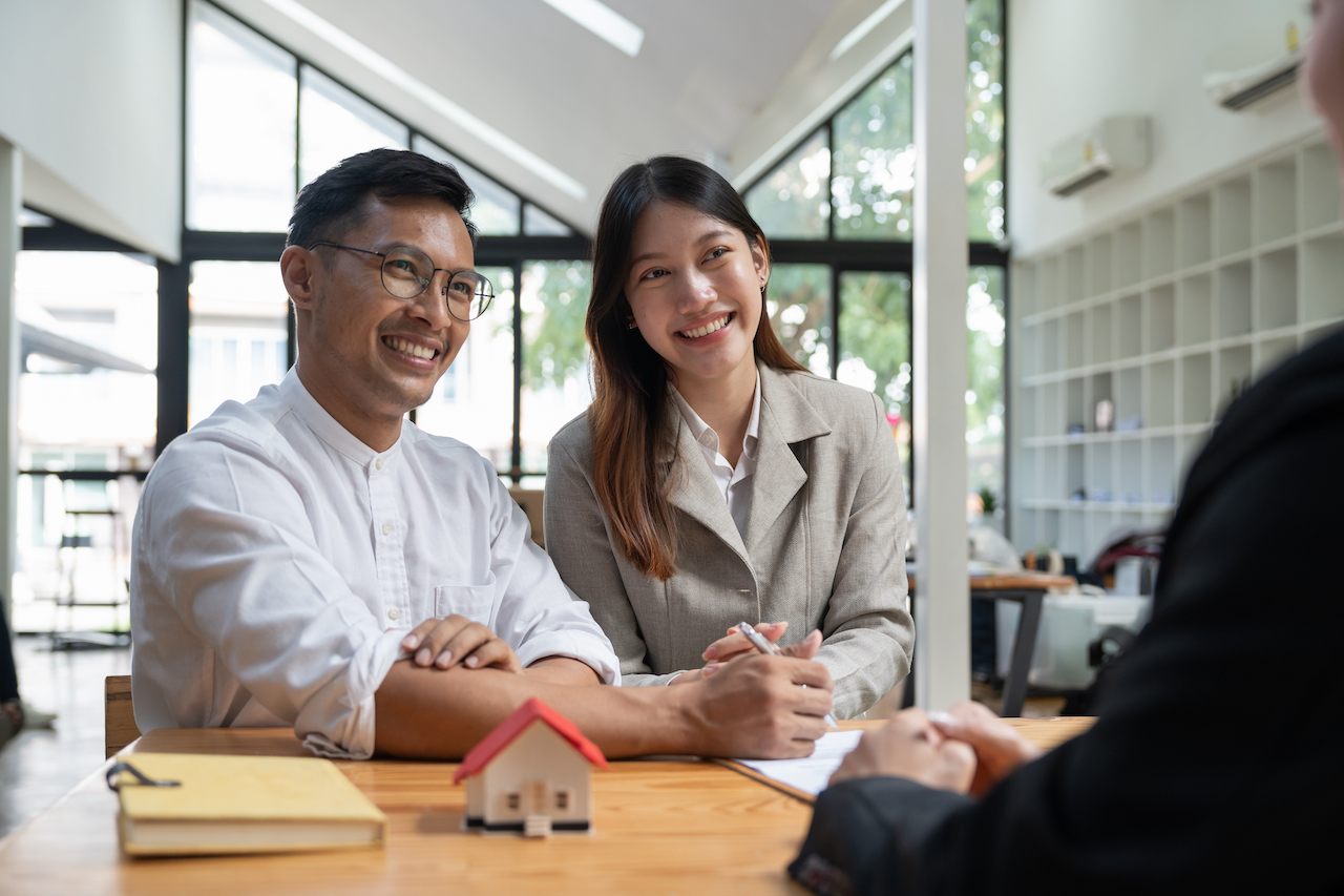 Happy property owners with real estate broker after a deal. Young couple handshaking real estate agent after signing contract