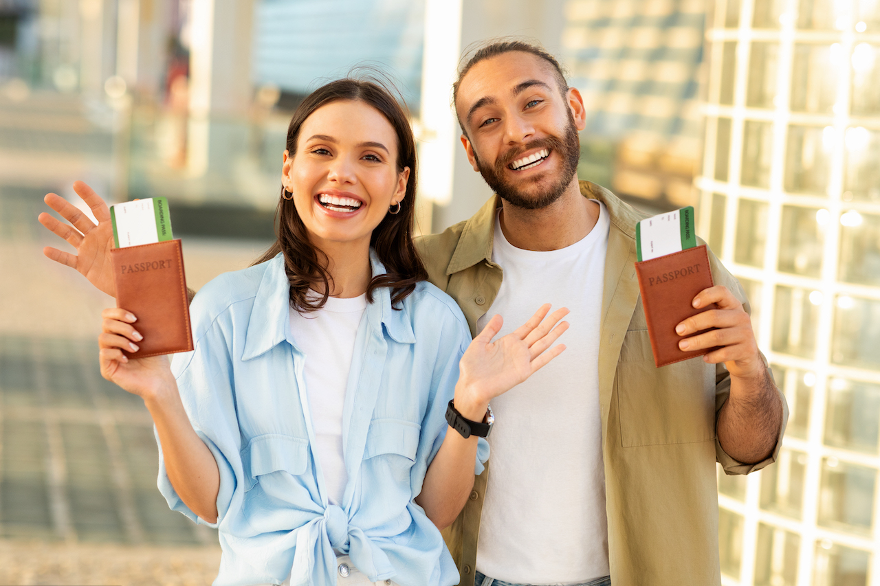 Happy young european guy with beard and woman hold passports and tickets, enjoy trip to station, outdoor. Tourist emotion, active lifestyle, travel at summer, vacation together